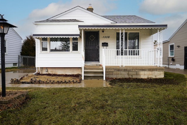 bungalow-style home featuring covered porch, roof with shingles, a front yard, and a chimney