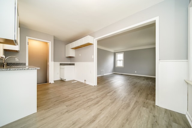 unfurnished living room with light wood-type flooring, visible vents, a sink, and wainscoting