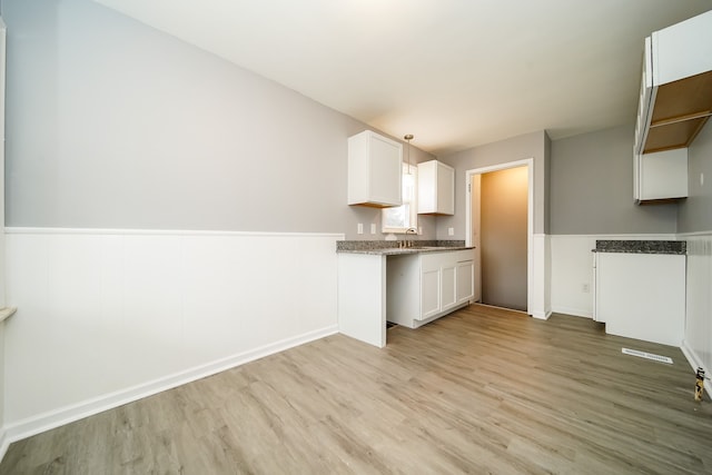 kitchen with a wainscoted wall, visible vents, white cabinetry, and light wood-style floors