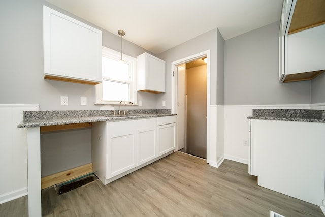 kitchen featuring light stone counters, a sink, white cabinets, light wood-style floors, and pendant lighting