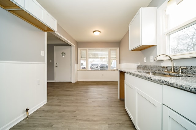 kitchen featuring light stone counters, light wood finished floors, wainscoting, white cabinetry, and a sink