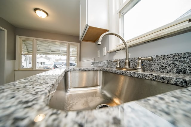 interior details featuring light stone counters, white cabinets, and a sink