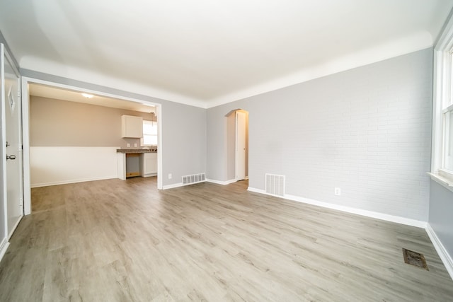 empty room with light wood finished floors, visible vents, and arched walkways