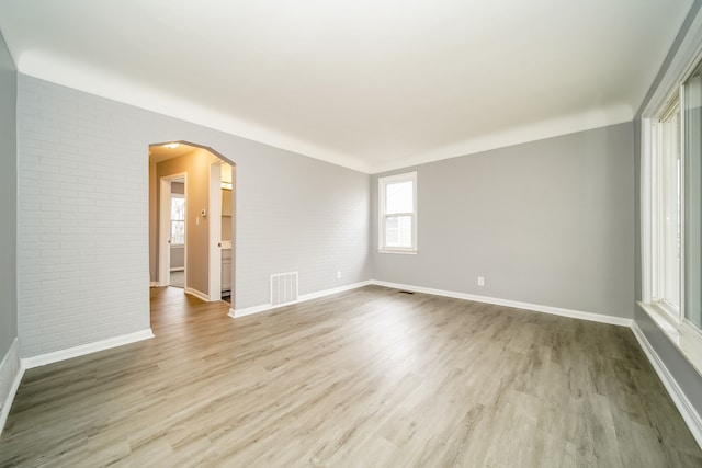 unfurnished room with brick wall, visible vents, arched walkways, and wood finished floors