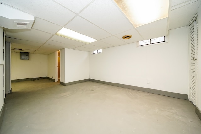 finished below grade area featuring visible vents, electric panel, a paneled ceiling, and baseboards