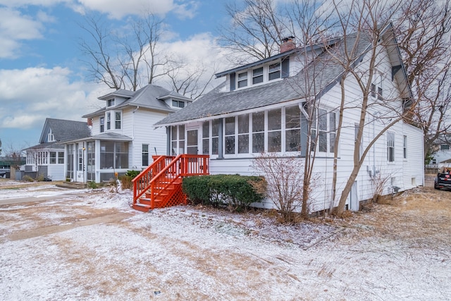 bungalow-style home featuring roof with shingles, a sunroom, and a chimney