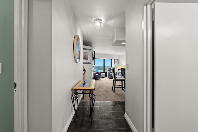 corridor featuring dark carpet and baseboards