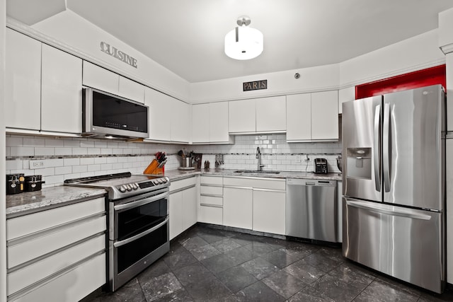 kitchen featuring light stone counters, backsplash, appliances with stainless steel finishes, white cabinetry, and a sink