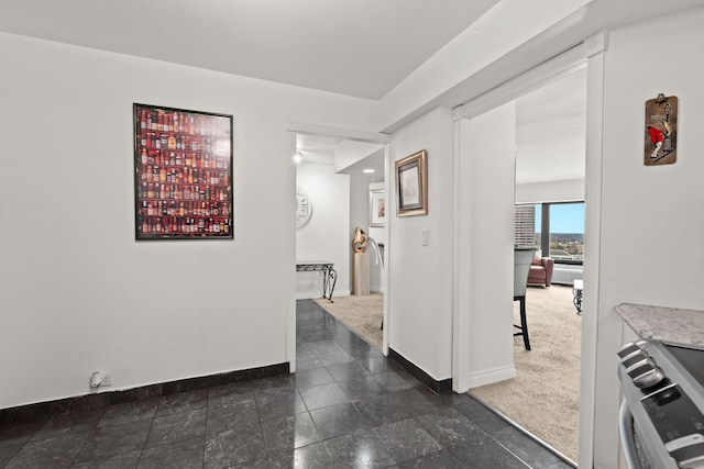 hallway featuring dark carpet and baseboards