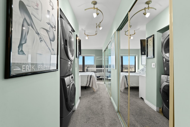 hallway featuring baseboards, carpet floors, track lighting, and stacked washer / drying machine