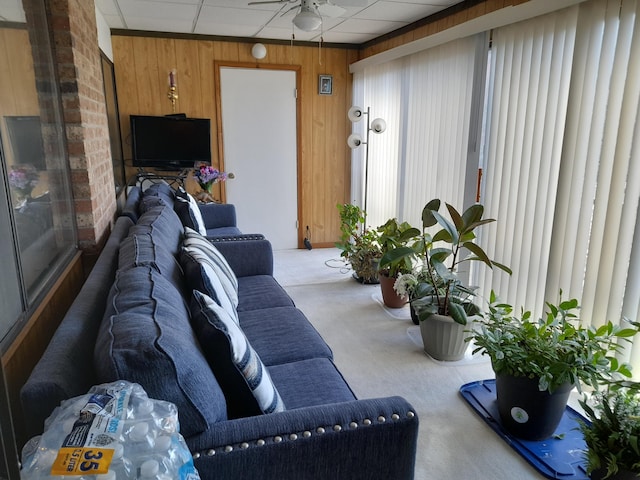 living area with carpet floors, a drop ceiling, wood walls, and ceiling fan