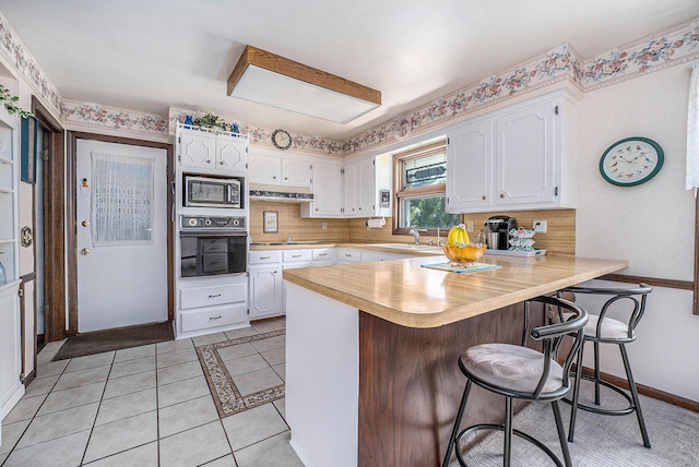 kitchen with stainless steel microwave, a peninsula, light countertops, white cabinetry, and black oven