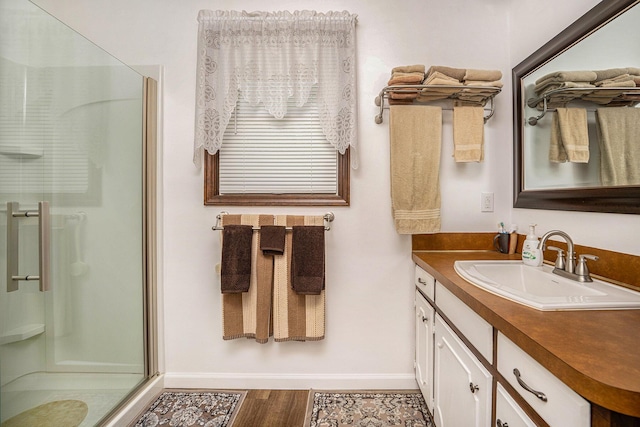 bathroom featuring wood finished floors, a shower stall, vanity, and baseboards