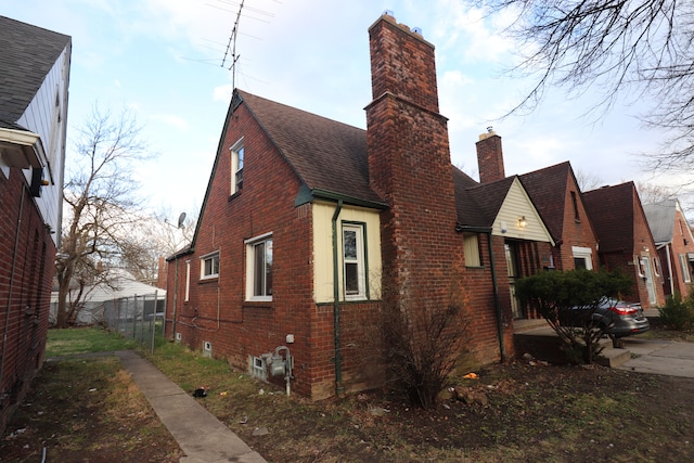 view of property exterior with fence, brick siding, roof with shingles, and a chimney