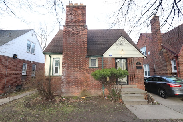 tudor house featuring brick siding, a chimney, and a shingled roof