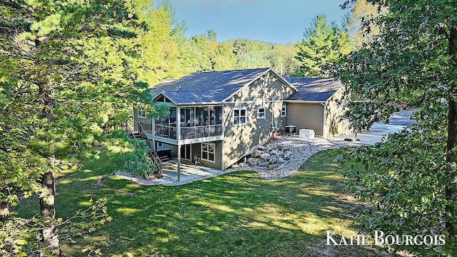 back of house featuring a sunroom, a patio area, a lawn, and a forest view