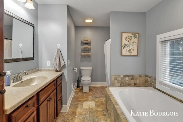 bathroom featuring tiled bath, baseboards, toilet, stone finish floor, and vanity