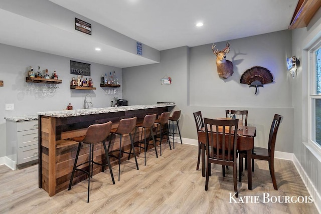 bar featuring light wood-style flooring, baseboards, indoor wet bar, and recessed lighting