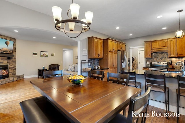 dining room featuring baseboards, wood finished floors, an inviting chandelier, a stone fireplace, and recessed lighting