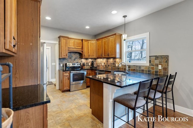 kitchen featuring tasteful backsplash, brown cabinetry, appliances with stainless steel finishes, a peninsula, and a sink