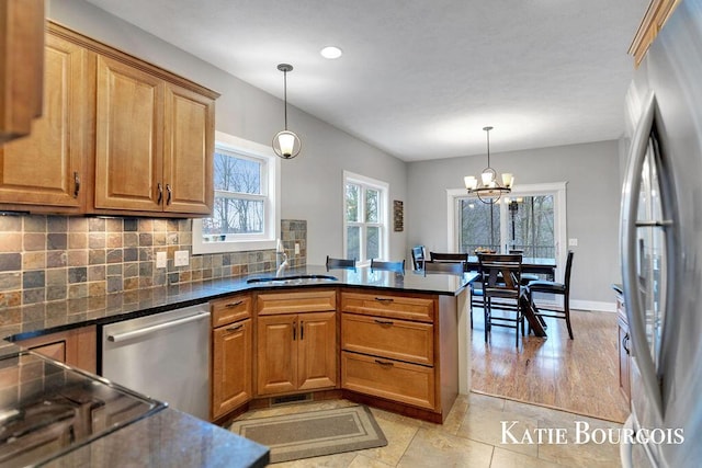 kitchen featuring tasteful backsplash, appliances with stainless steel finishes, brown cabinetry, a sink, and a peninsula