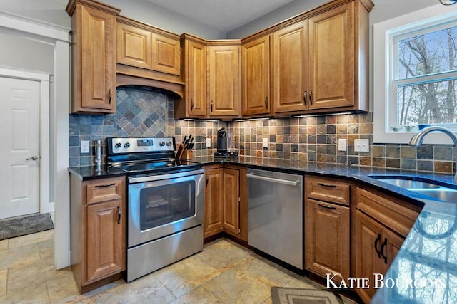 kitchen with brown cabinets, stainless steel appliances, decorative backsplash, a sink, and dark stone countertops