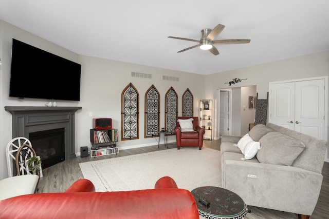 living area featuring a ceiling fan, a glass covered fireplace, visible vents, and wood finished floors