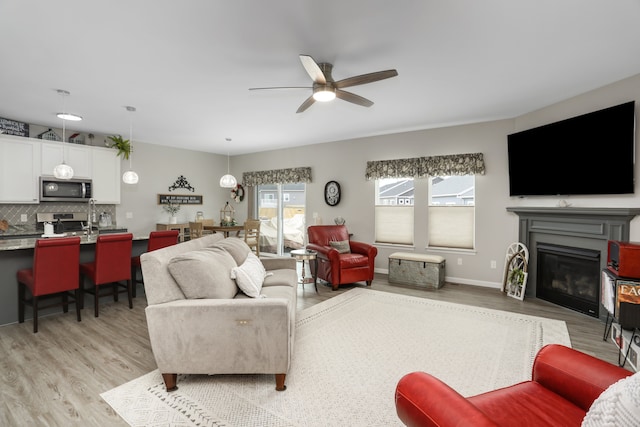 living area featuring light wood finished floors, baseboards, a ceiling fan, and a glass covered fireplace