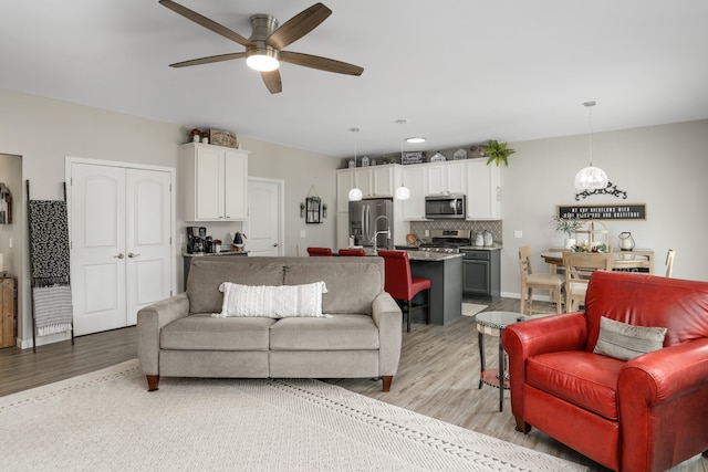 living room with ceiling fan, baseboards, and light wood-style floors