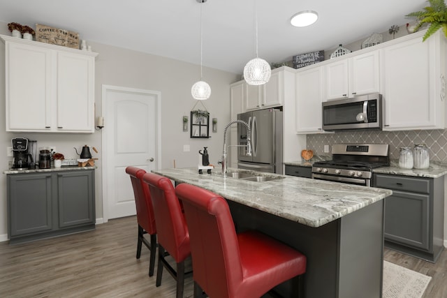 kitchen with tasteful backsplash, appliances with stainless steel finishes, gray cabinetry, light wood-style floors, and a sink