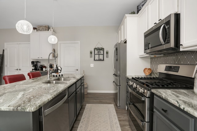 kitchen featuring appliances with stainless steel finishes, white cabinets, a kitchen island with sink, a sink, and light stone countertops