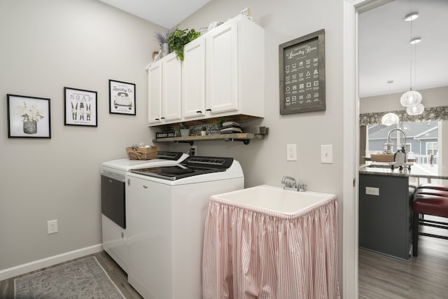 laundry area with a sink, wood finished floors, baseboards, cabinet space, and washer and clothes dryer