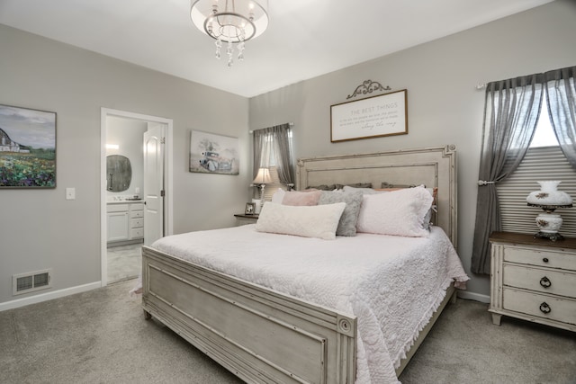 carpeted bedroom with visible vents, a notable chandelier, ensuite bath, and baseboards