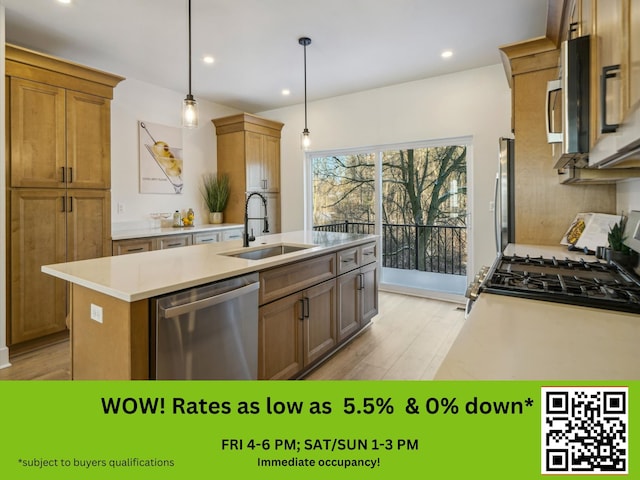 kitchen featuring a center island with sink, light wood finished floors, stainless steel appliances, light countertops, and a sink