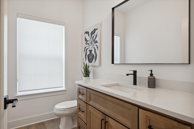 bathroom featuring toilet, baseboards, wood finished floors, and vanity