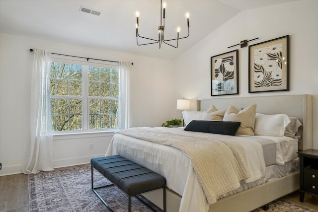 bedroom with baseboards, visible vents, lofted ceiling, wood finished floors, and a chandelier