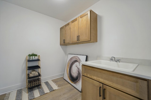 clothes washing area featuring baseboards, cabinet space, a sink, and light wood finished floors