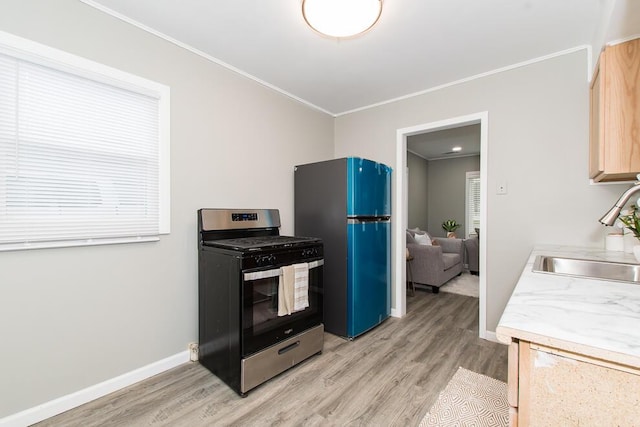 kitchen featuring ornamental molding, freestanding refrigerator, a sink, light wood-type flooring, and stainless steel gas range oven