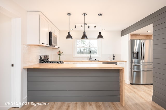 kitchen featuring a peninsula, appliances with stainless steel finishes, a sink, and wooden counters