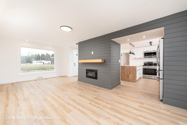 unfurnished living room featuring light wood-type flooring, baseboards, a fireplace, and visible vents