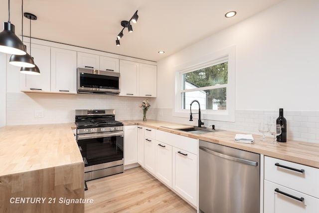 kitchen with white cabinets, butcher block counters, stainless steel appliances, and a sink