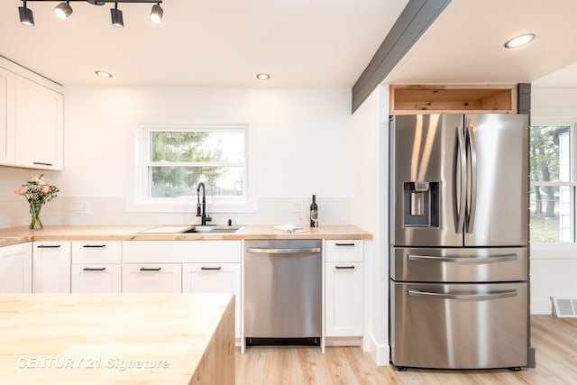 kitchen with wooden counters, appliances with stainless steel finishes, a sink, and tasteful backsplash