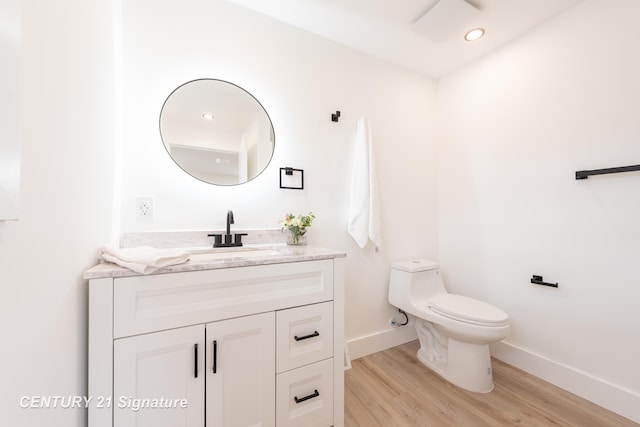 half bathroom featuring baseboards, toilet, wood finished floors, vanity, and recessed lighting