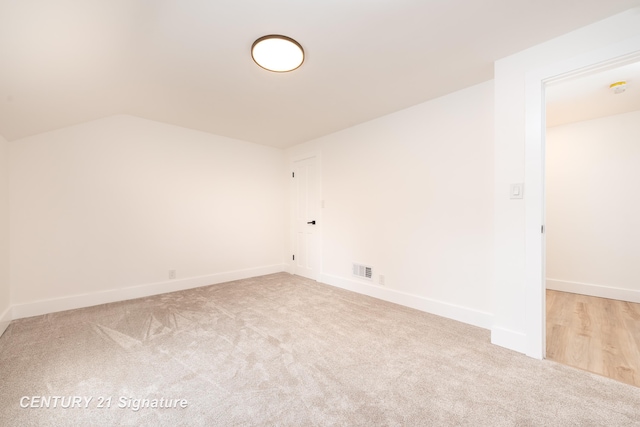 spare room featuring carpet floors, baseboards, visible vents, and vaulted ceiling