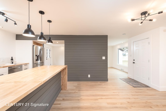 kitchen featuring decorative light fixtures, wooden counters, appliances with stainless steel finishes, white cabinets, and light wood-type flooring