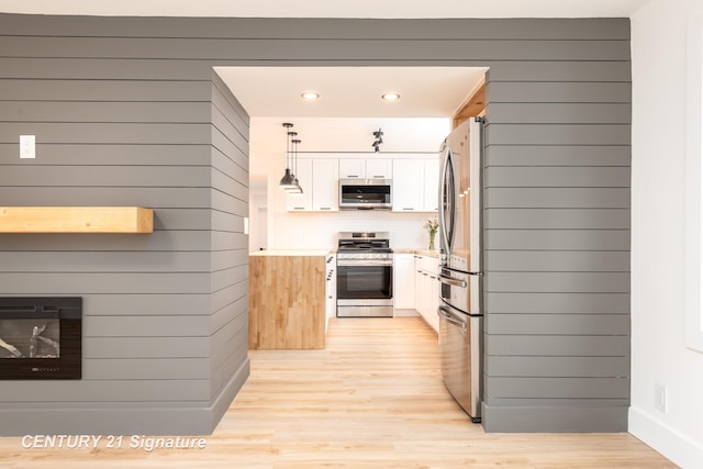 kitchen featuring light wood-style flooring, a fireplace, white cabinetry, appliances with stainless steel finishes, and decorative light fixtures