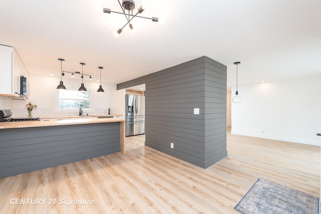 kitchen featuring appliances with stainless steel finishes, light wood-type flooring, a sink, and a peninsula