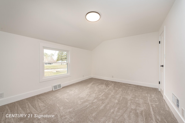 carpeted empty room featuring vaulted ceiling, visible vents, and baseboards