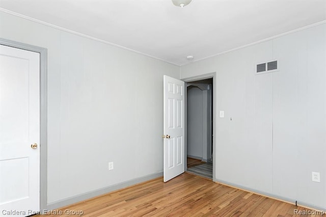 empty room with light wood finished floors, visible vents, and crown molding