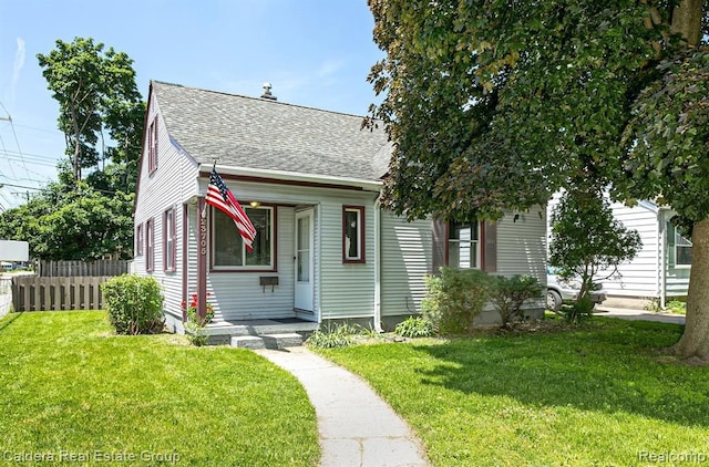 view of front facade featuring a front lawn, a shingled roof, and fence